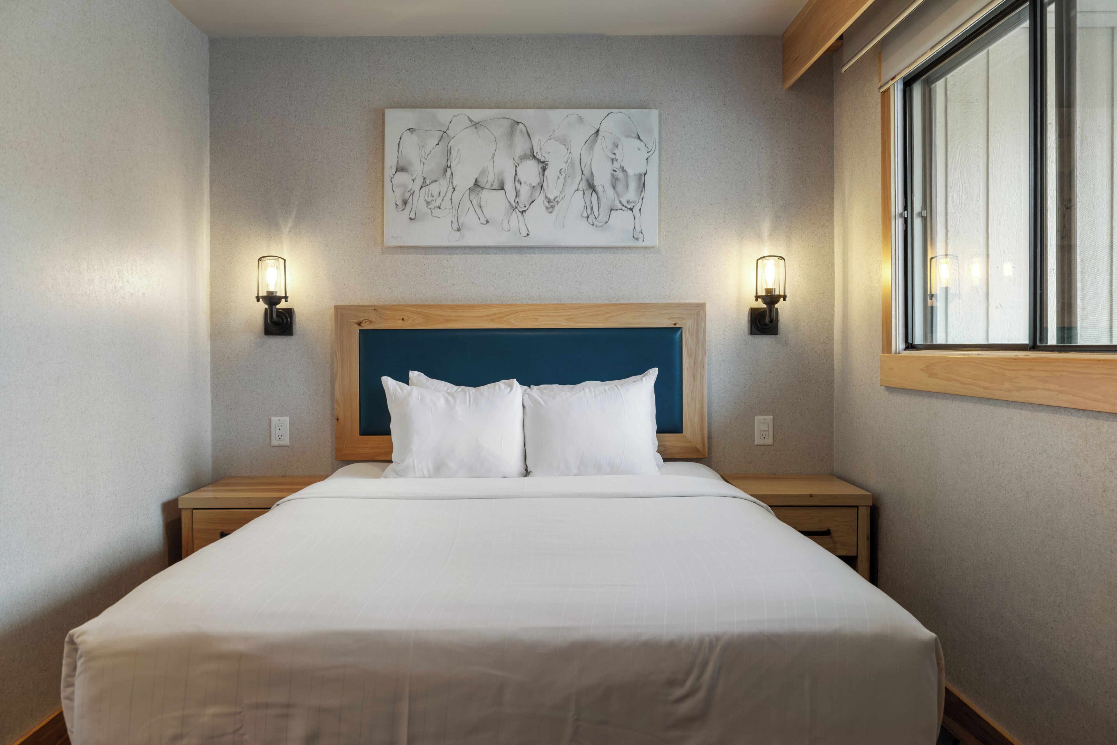 A hotel room with a large bed, two bedside tables, a headboard, and a window.
