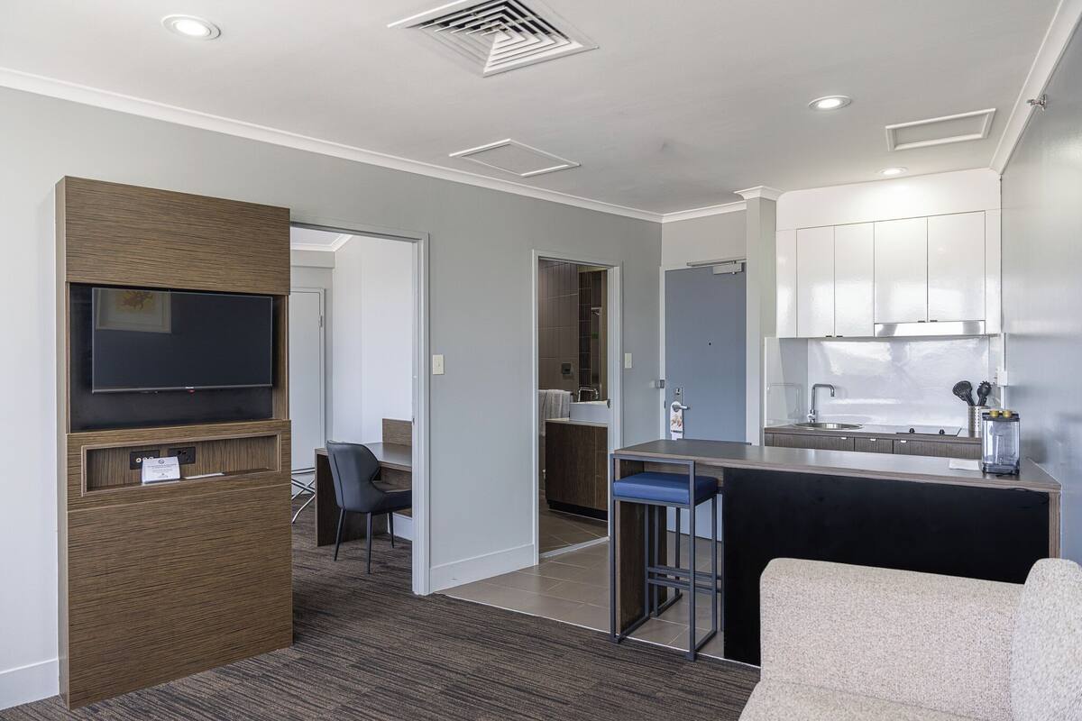 Une chambre d’hôtel moderne dotée d’une kitchenette, d’un téléviseur à écran plat, d’un coin salon et d’une porte donnant accès à la salle de bain.