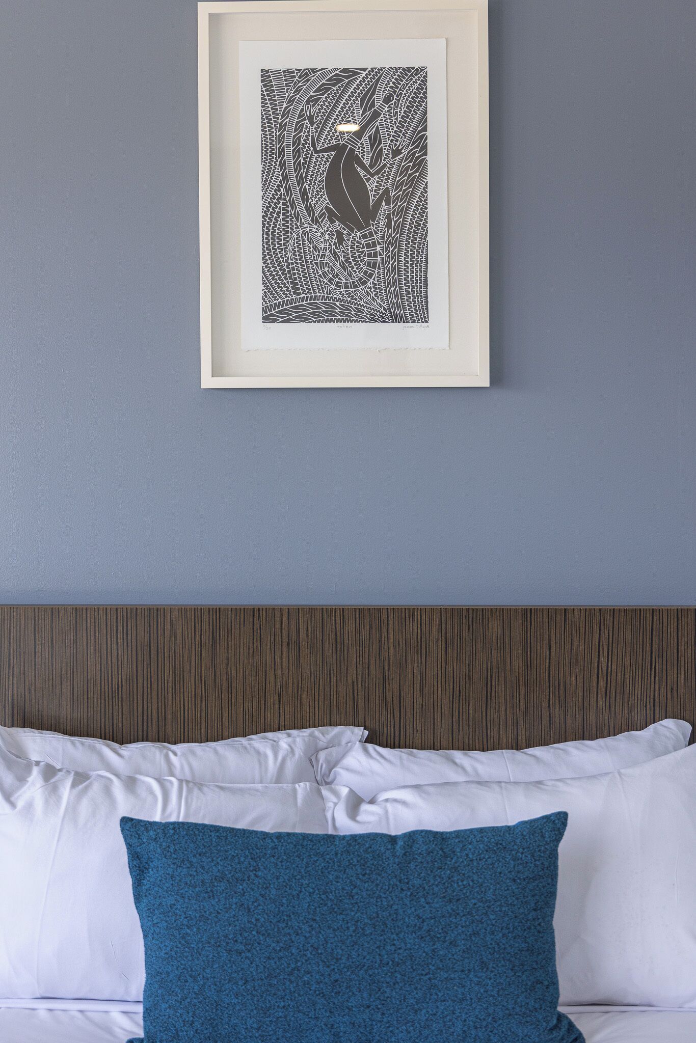 Une œuvre d’art encadrée accrochée au mur, un lit avec des oreillers blancs et bleus, et une tête de lit en bois.