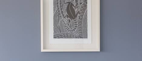 Une œuvre d’art encadrée accrochée au mur, un lit avec des oreillers blancs et bleus, et une tête de lit en bois.