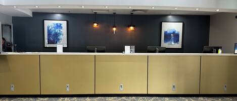 A reception area with a counter, two framed artworks, pendant lighting, and a patterned carpet.
