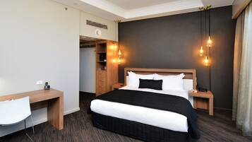 Ein Hotelzimmer mit einem großen Bett, einem Schreibtisch mit Stuhl, einem Kleiderschrank und einem Nachttisch.