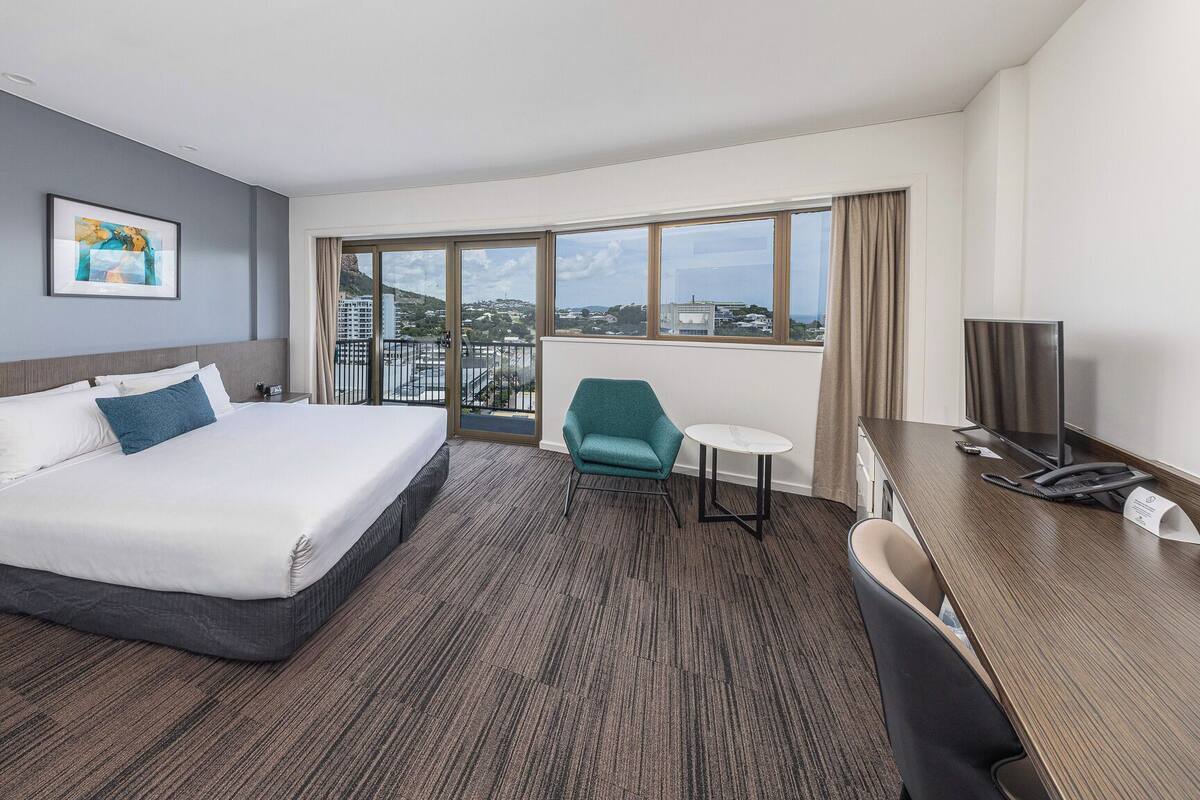 Une chambre d’hôtel avec un grand lit, un bureau avec un téléphone, une chaise, une petite table et un téléviseur.