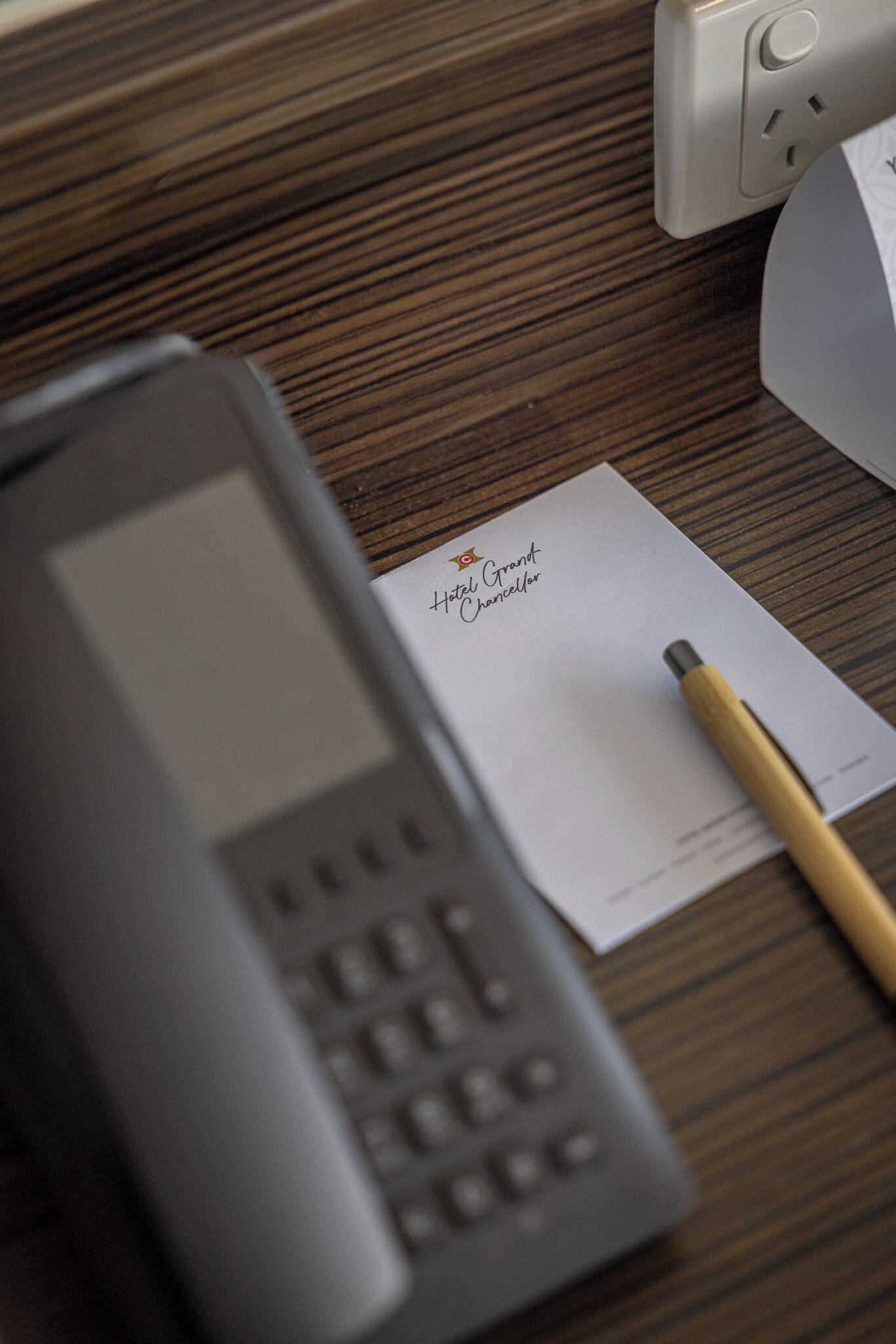 A hotel room with a wooden desk, a telephone, a pen, and a business card.