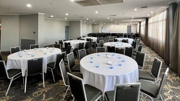 Un salón de conferencias con varias mesas redondas, sillas y piso alfombrado.