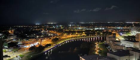 A nighttime cityscape with a river, illuminated bridge, and modern buildings.