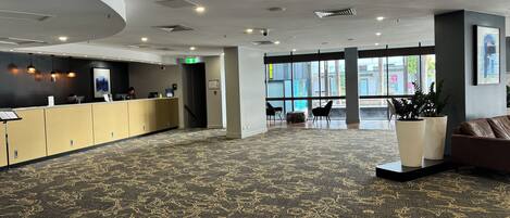 A spacious lobby with a reception desk, seating area, and large windows offering a view of the street.