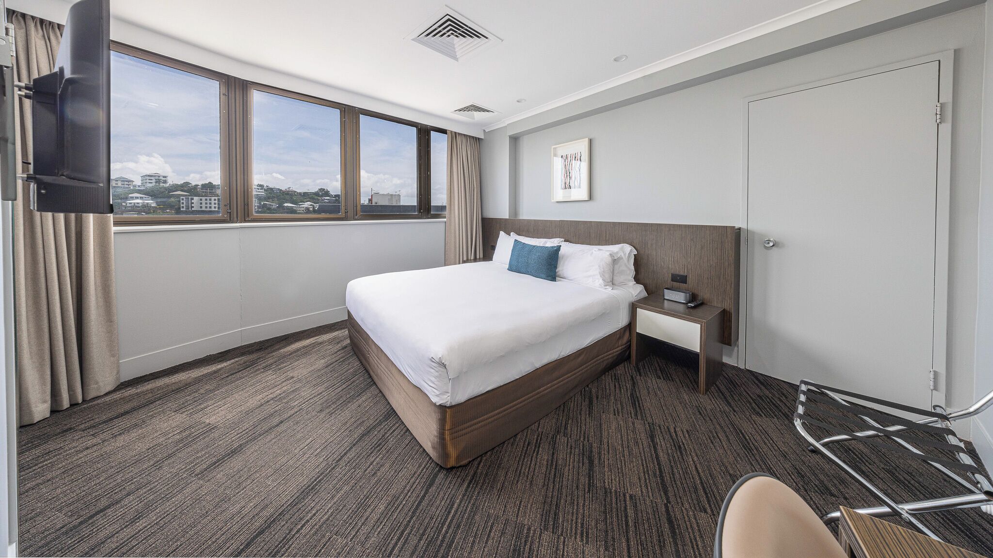 Een hotelkamer met een groot bed, een nachtkastje, een televisie en uitzicht op de stad.