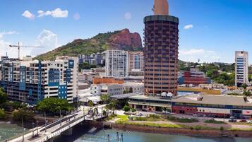 A coastal cityscape with modern buildings, a prominent cylindrical tower, and a bridge over a calm body of water.