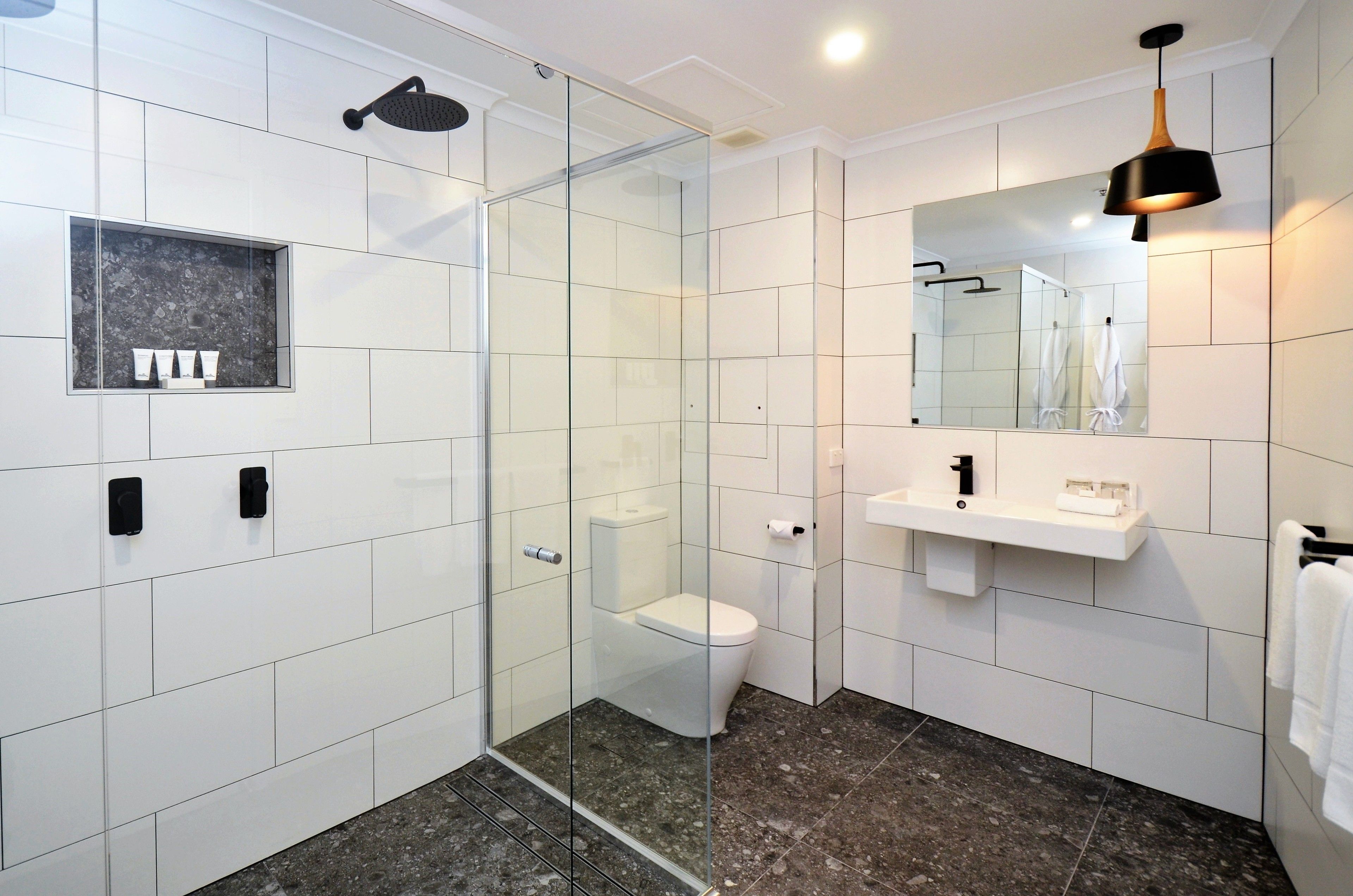 A modern bathroom with a glass-enclosed shower, a white toilet, a vanity with a mirror, and a towel rack.