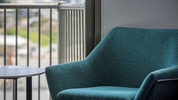 A teal armchair and a small table on a balcony with a view of buildings and greenery.