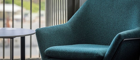 Un sillón azul aguamarina y una pequeña mesa en un balcón con vistas a edificios y follaje.