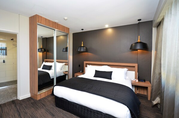 Ein modernes Hotelzimmer mit einem großen Bett, einem Spiegel, zwei Nachttischen und Pendelleuchten.