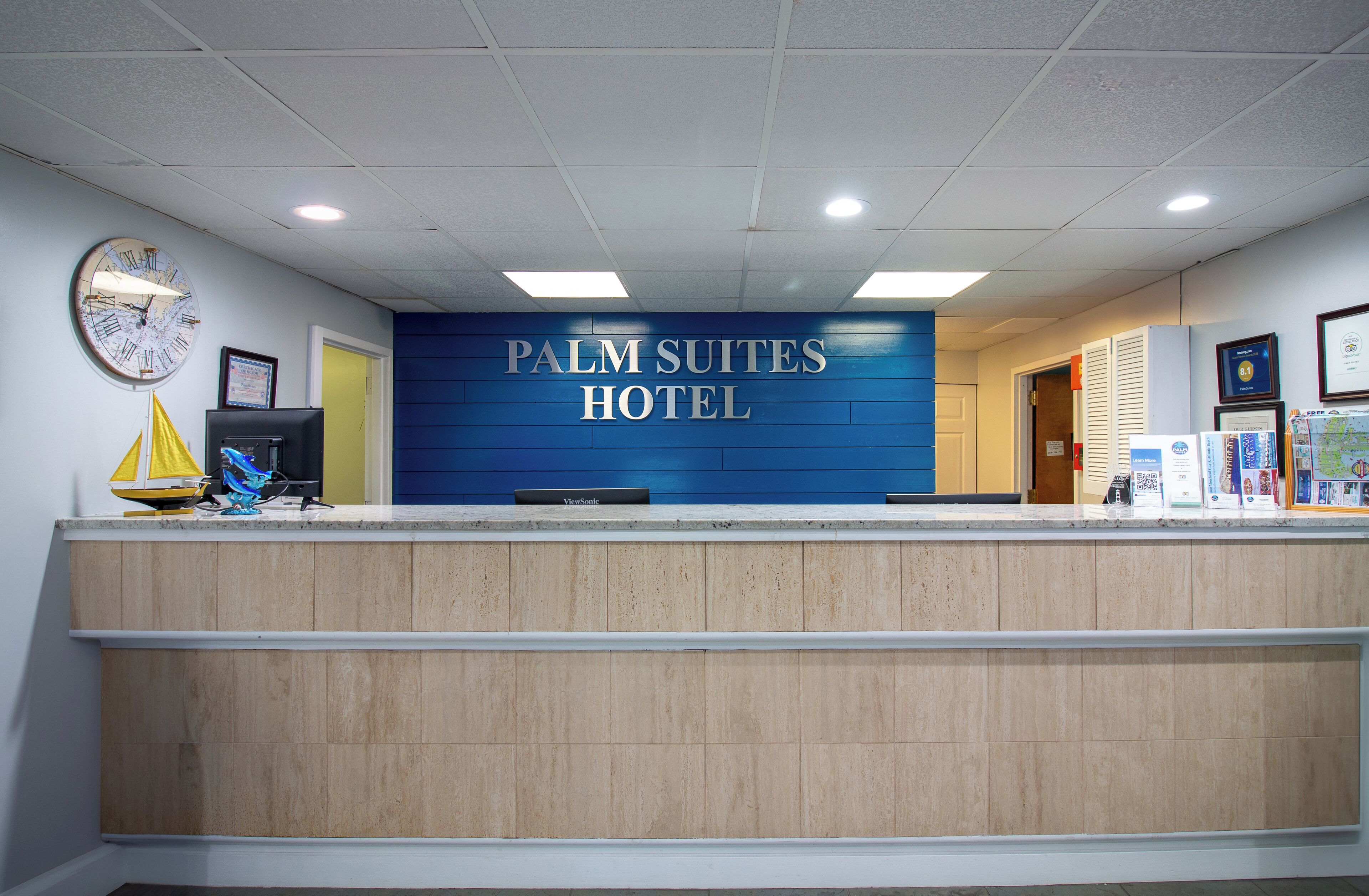 A reception desk with a sign reading "PALM SUITES HOTEL" and a clock on the wall.
