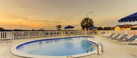 A swimming pool with lounge chairs and umbrellas, surrounded by a white fence.