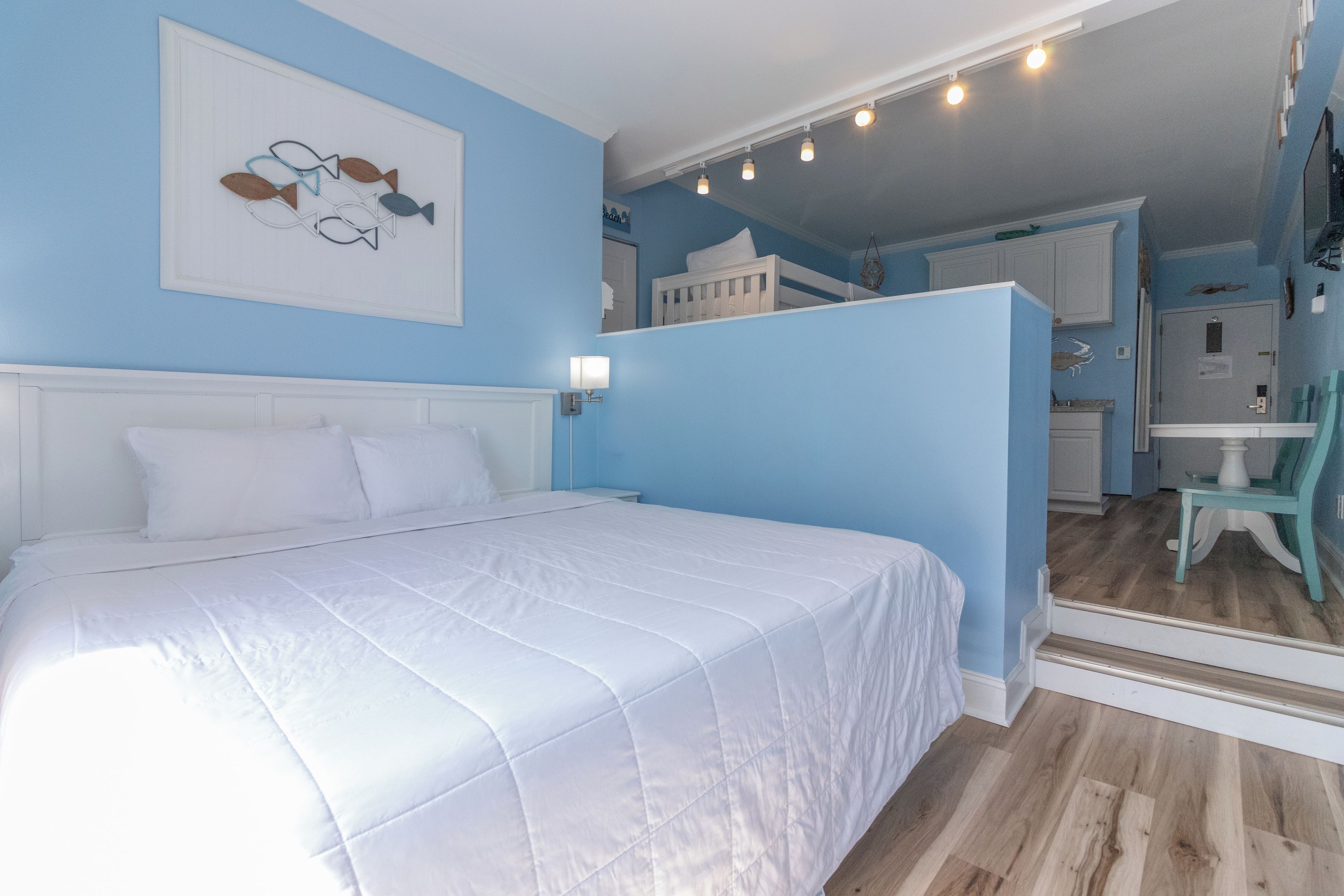 Une chambre à coucher comprenant un lit, une table de chevet, une lampe fixée au mur et une porte donnant sur une salle de bain.