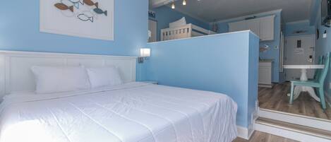 Une chambre à coucher comprenant un lit, une table de chevet, une lampe fixée au mur et une porte donnant sur une salle de bain.