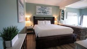 A bedroom with a large bed, two bedside tables, a nightstand, a potted plant, and a stone accent wall. - Palm Suites Trademark Collection by Wyndham (Atlantic Beach)
