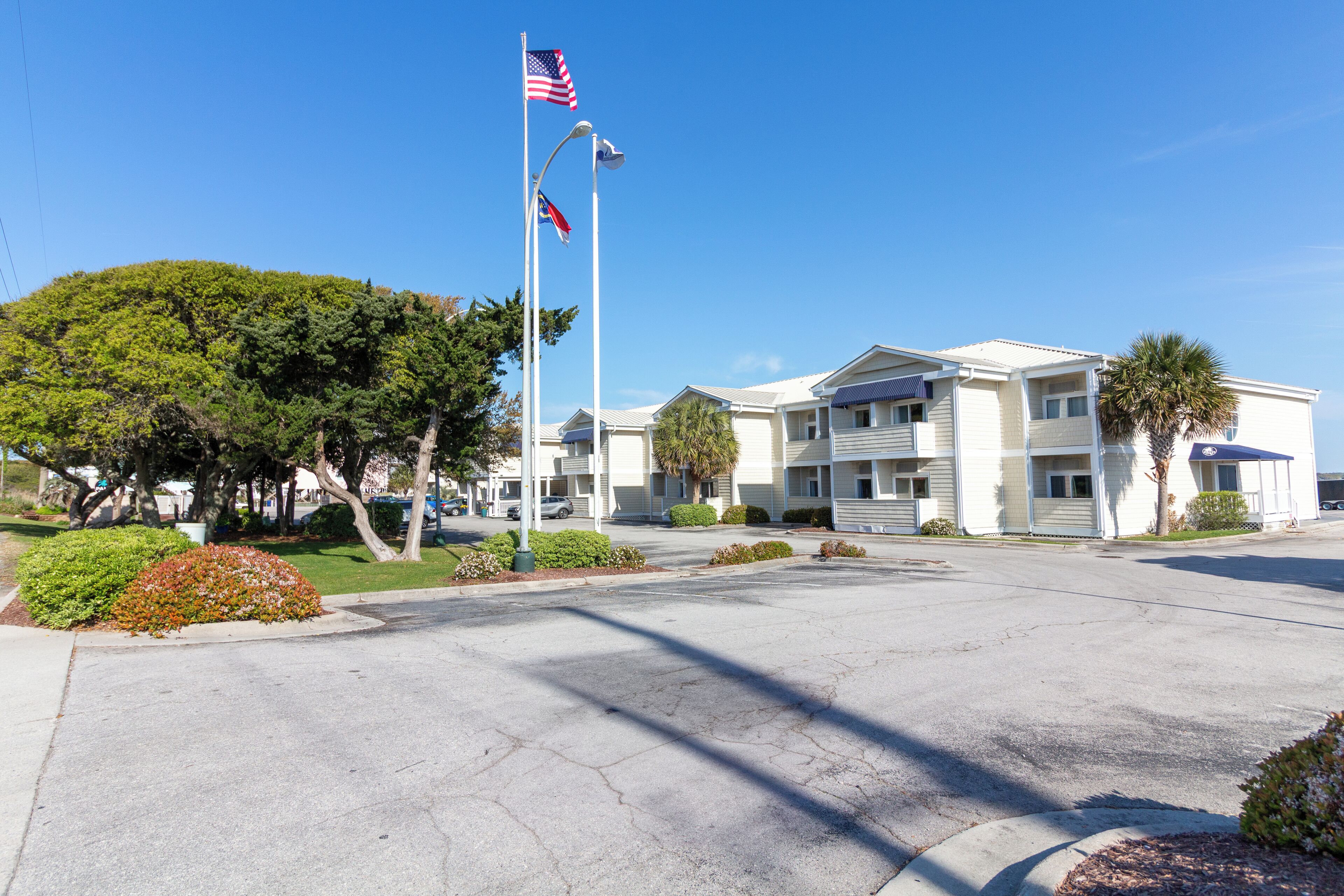 Un hôtel à plusieurs étages doté d’un parking, d’un mât portant des drapeaux américains et d’un aménagement paysager bien entretenu.