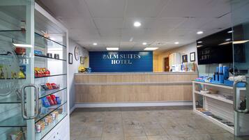 A reception area with a blue sign reading "PALM SUITES HOTEL" and a glass display case with snacks.