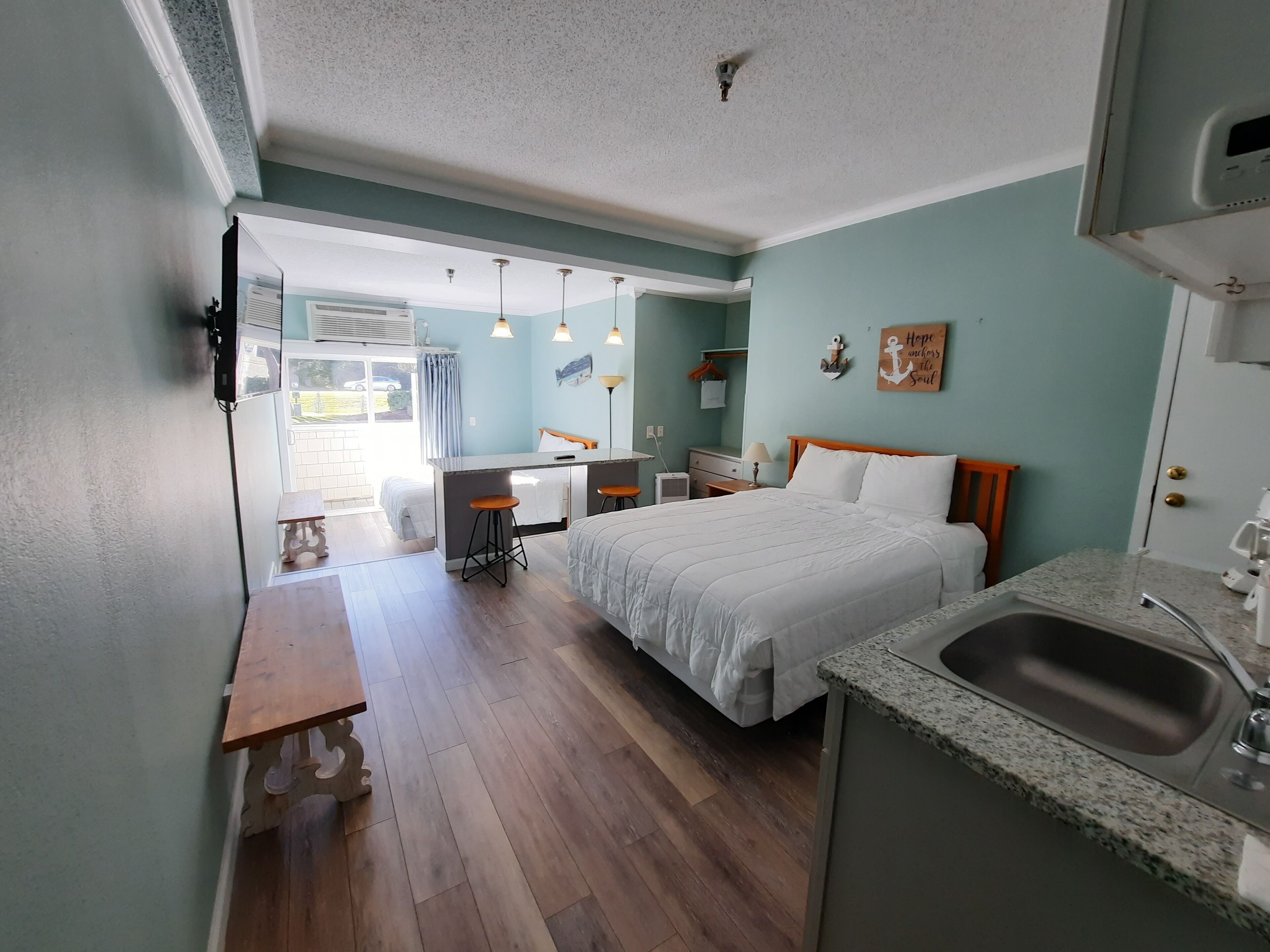 Une chambre d’hôtel de taille réduite, comprenant un lit, un petit bureau, une kitchenette et une salle de bain.