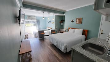A compact hotel room with a bed, a small desk, a kitchenette, and a bathroom.