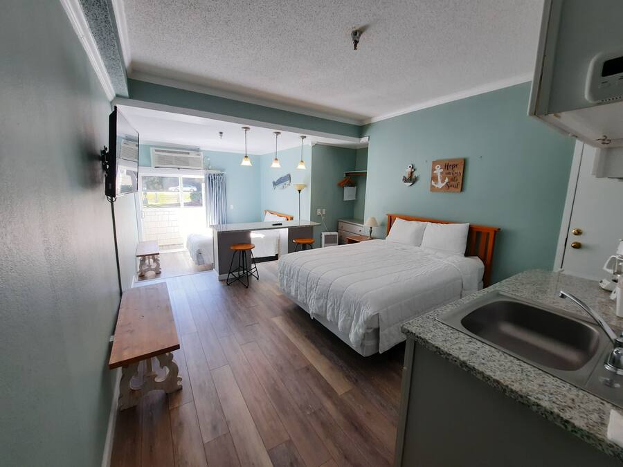 A compact hotel room with a bed, a small desk, a kitchenette, and a bathroom.