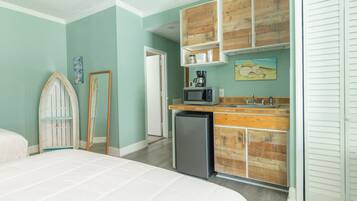 Un dormitorio con cama, una kitchenette pequeña con microondas y un refrigerador. Hay un mueble de madera sobre el lavamanos y una puerta con espejo.