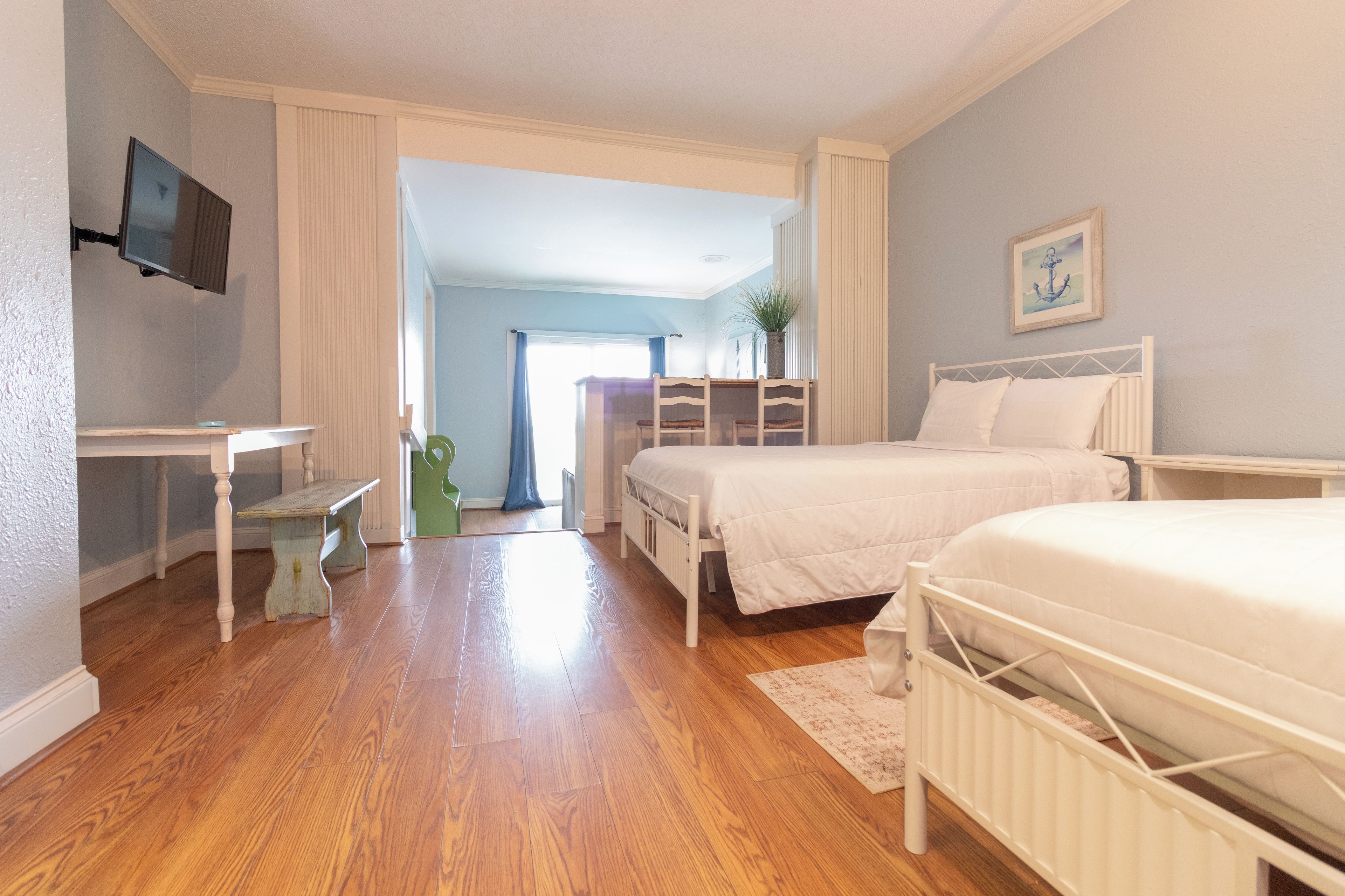 A bedroom with two beds, a desk, a chair, a TV, and a painting.