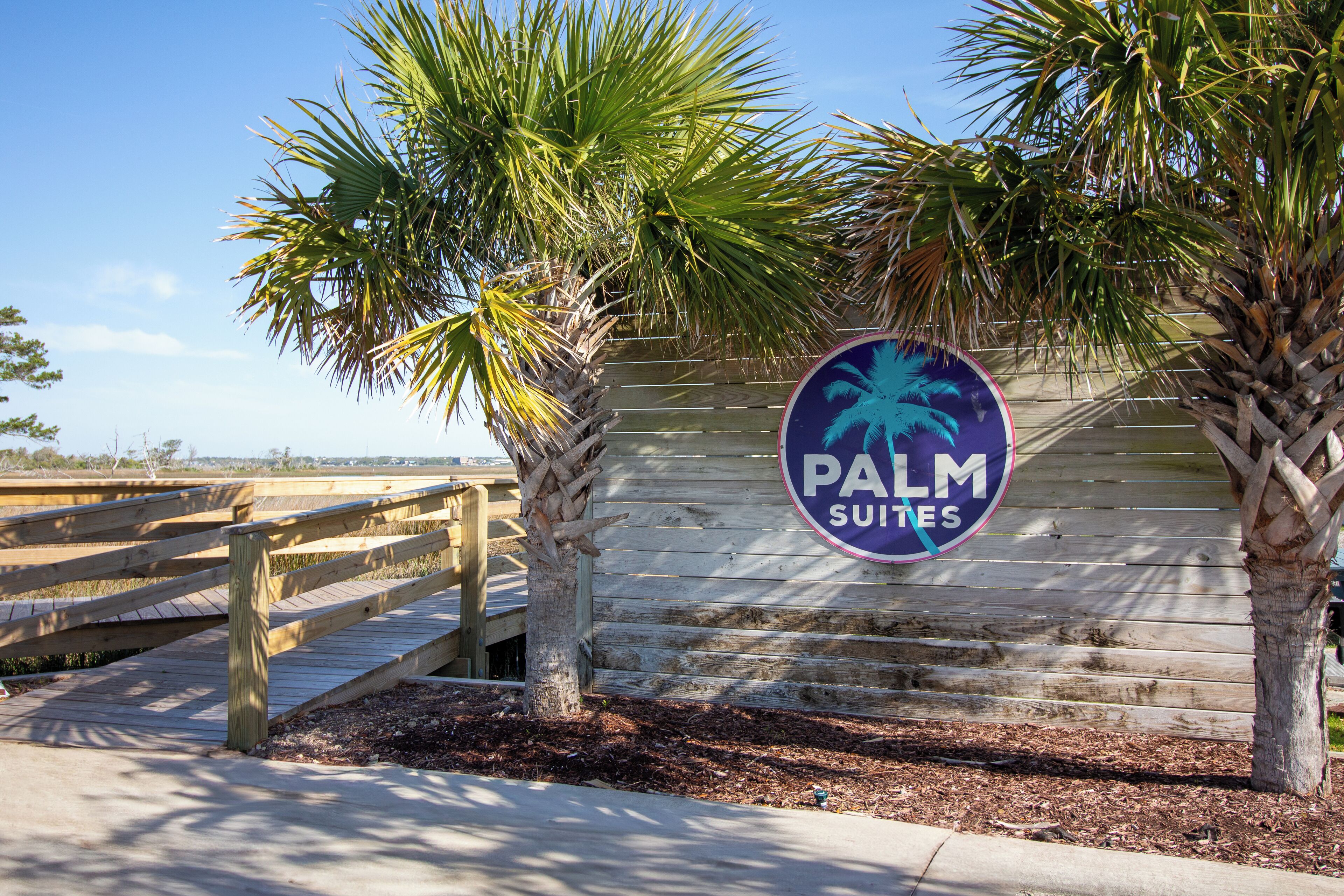 Un paseo marítimo de madera que conduce a un letrero de Palm Suites.