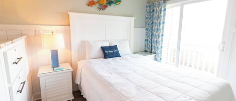 A bedroom with a bed, a nightstand with a lamp, a dresser, and a wall decoration.