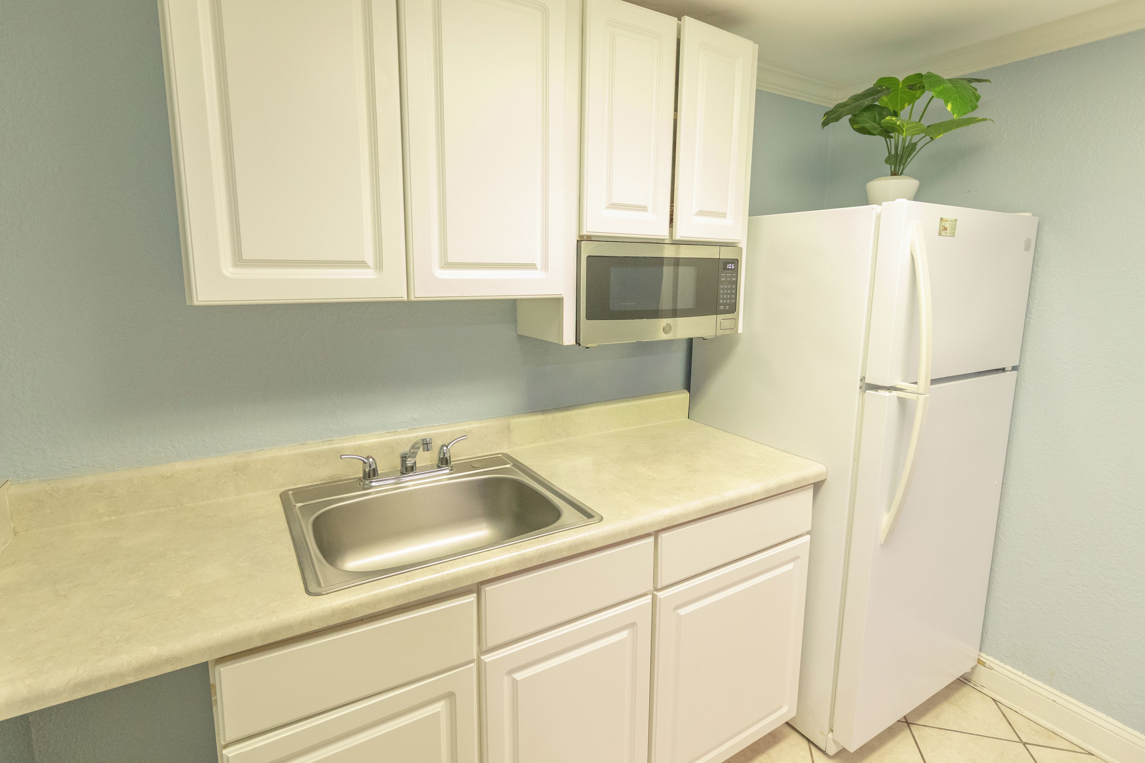 Una cocina con armarios blancos, un lavamanos de acero inoxidable, un microondas y un refrigerador.