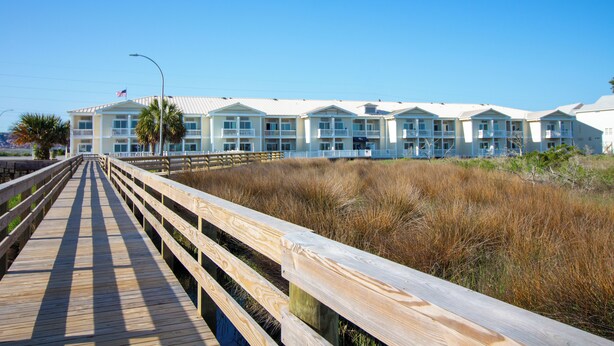 A row of white buildings with balconies, a wooden boardwalk, and tall grass in the foreground. - Palm Suites Trademark Collection by Wyndham (Atlantic Beach)