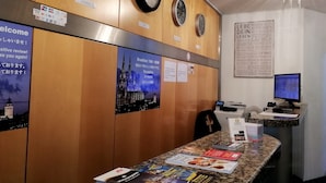 A reception desk with clocks, a poster of a cathedral, and a computer monitor. - Hotel Königshof The Arthouse (Cologne)