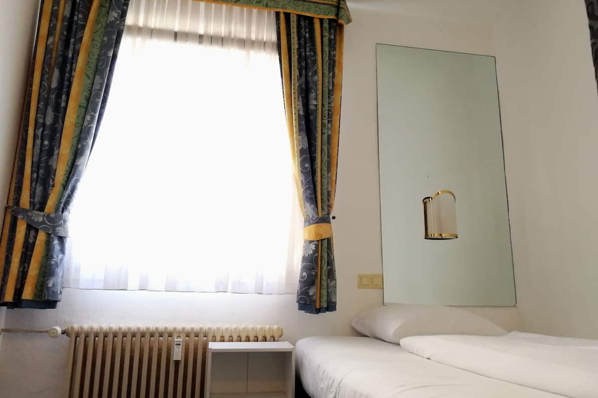 Une chambre d’hôtel avec un lit, un radiateur et des rideaux.