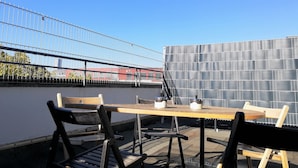 An outdoor seating area with a table and chairs, a metal fence, and a building in the background. - Hotel Königshof The Arthouse (Cologne)