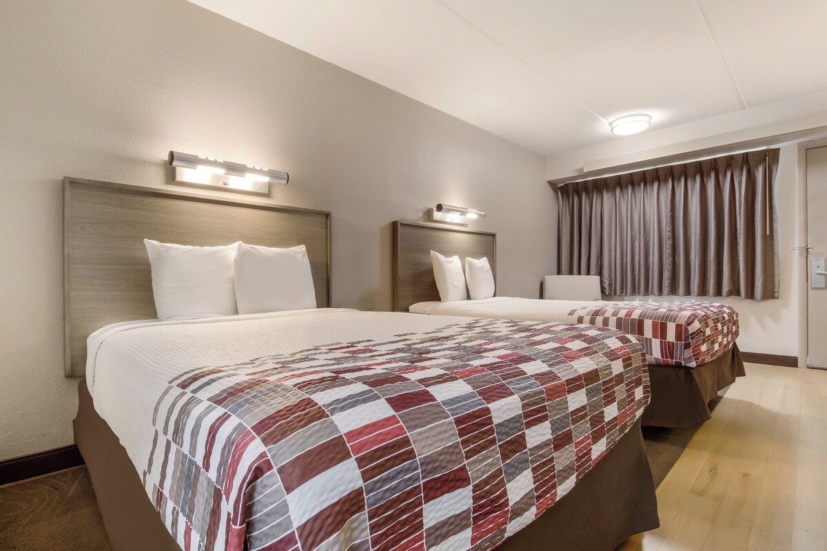 A hotel room with two beds, each with a headboard and bedside lamps.