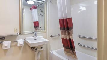 A bathroom with a white sink, a mirror, a shower with a red and white curtain, and a bathtub.