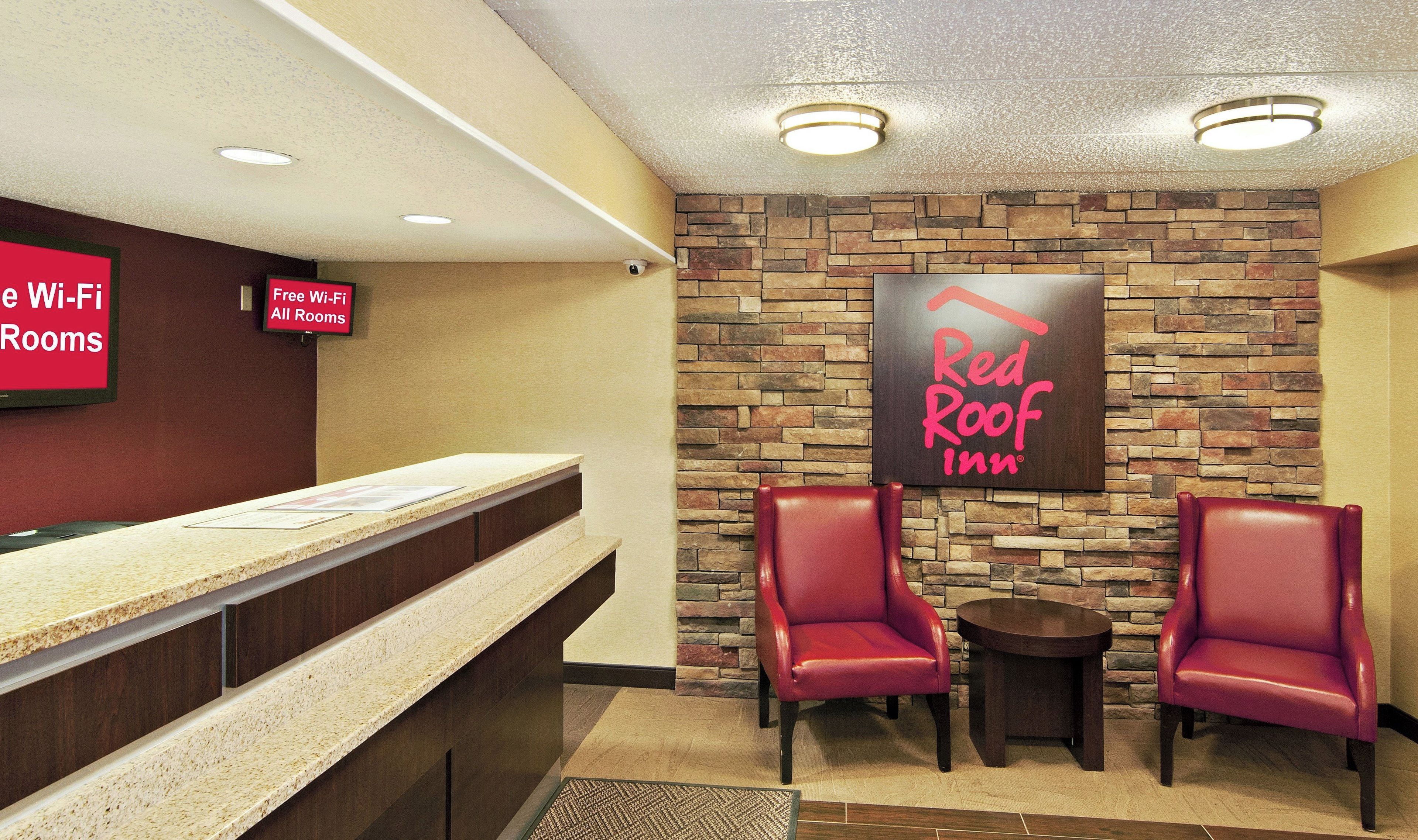 Zona de recepción de Red Roof Inn con pared de piedra, dos sillones de cuero, un mostrador de recepción y un letrero que indica Wi-Fi gratuito en todas las habitaciones.