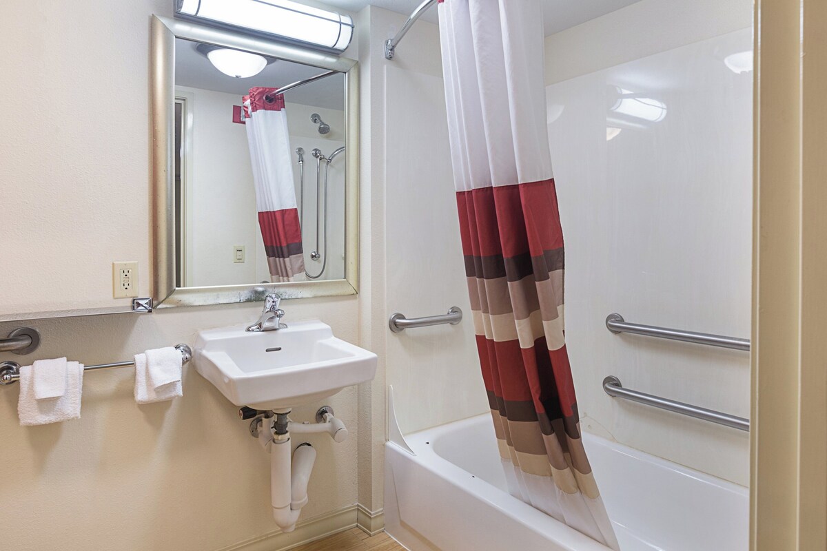 A bathroom with a sink, mirror, shower, and a red and white striped shower curtain.