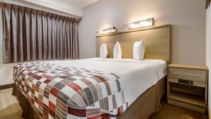 A hotel room with a large bed, a wooden headboard, a nightstand with a drawer, and a window with curtains. - Red Roof Inn Detroit - Farmington Hills (Farmington Hills)
