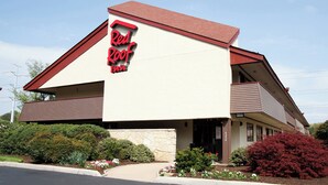 A Red Roof Inn with a red and white facade, a stone foundation, and a balcony on the second floor. - Red Roof Inn Detroit - Farmington Hills (Farmington Hills)