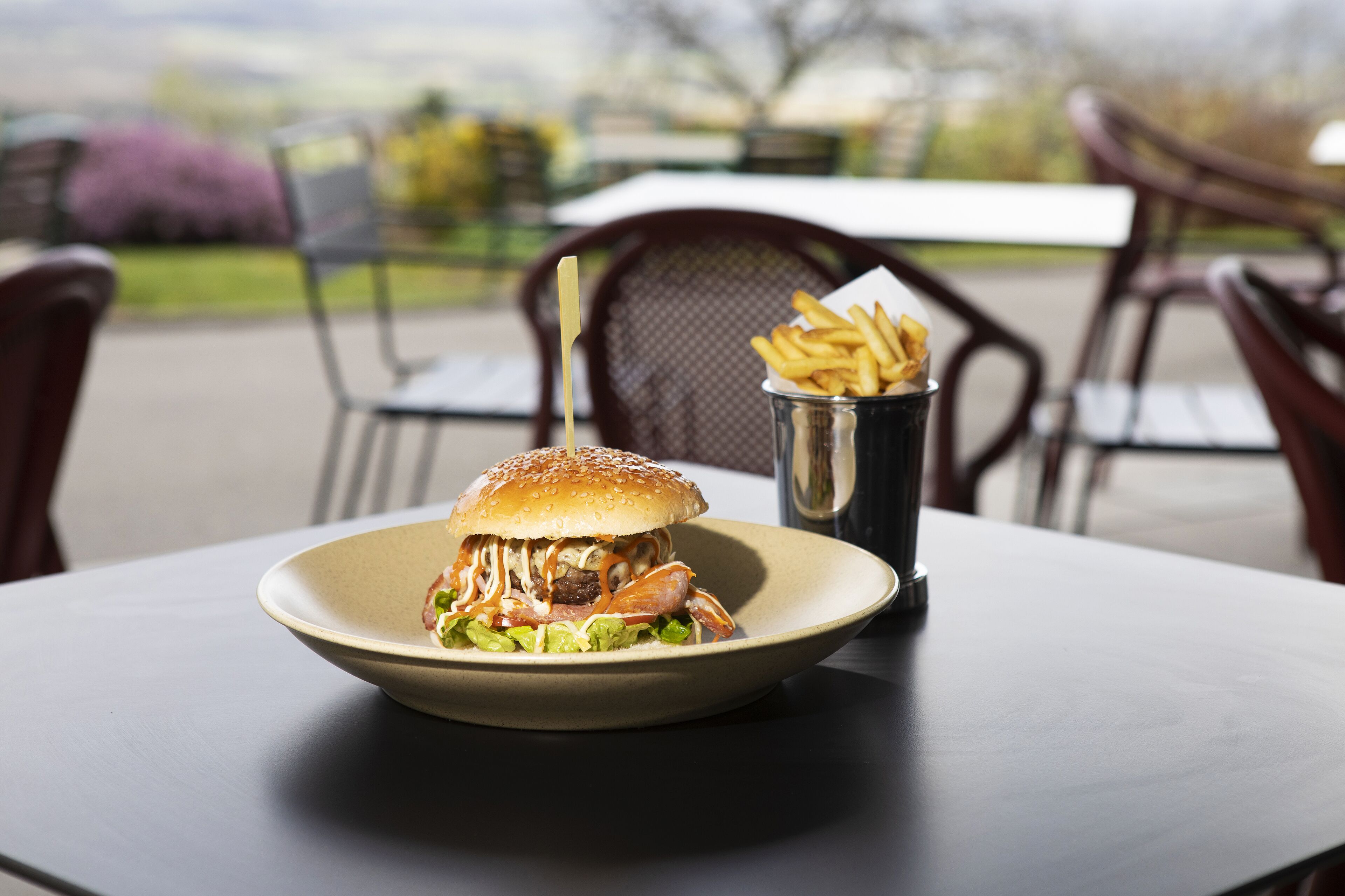 Ein Burger mit Pommes auf einem Tisch, rundherum Stühle.