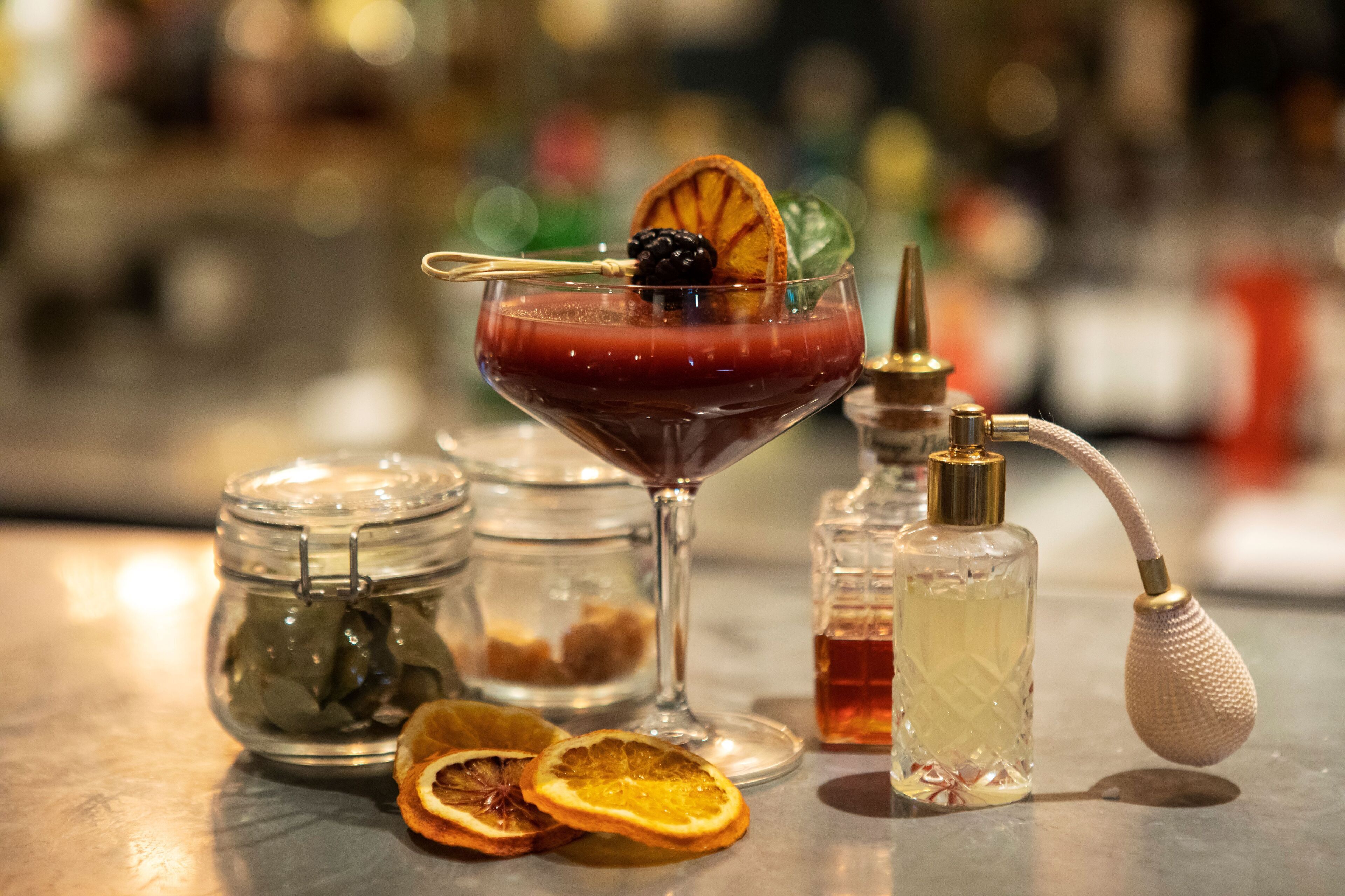 A bar setting with a martini glass, a bottle of liquor, and a jar of pickles.
