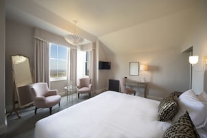 Habitación de hotel con una cama grande, dos sillones, una mesita, un escritorio, un televisor y una ventana con cortinas.