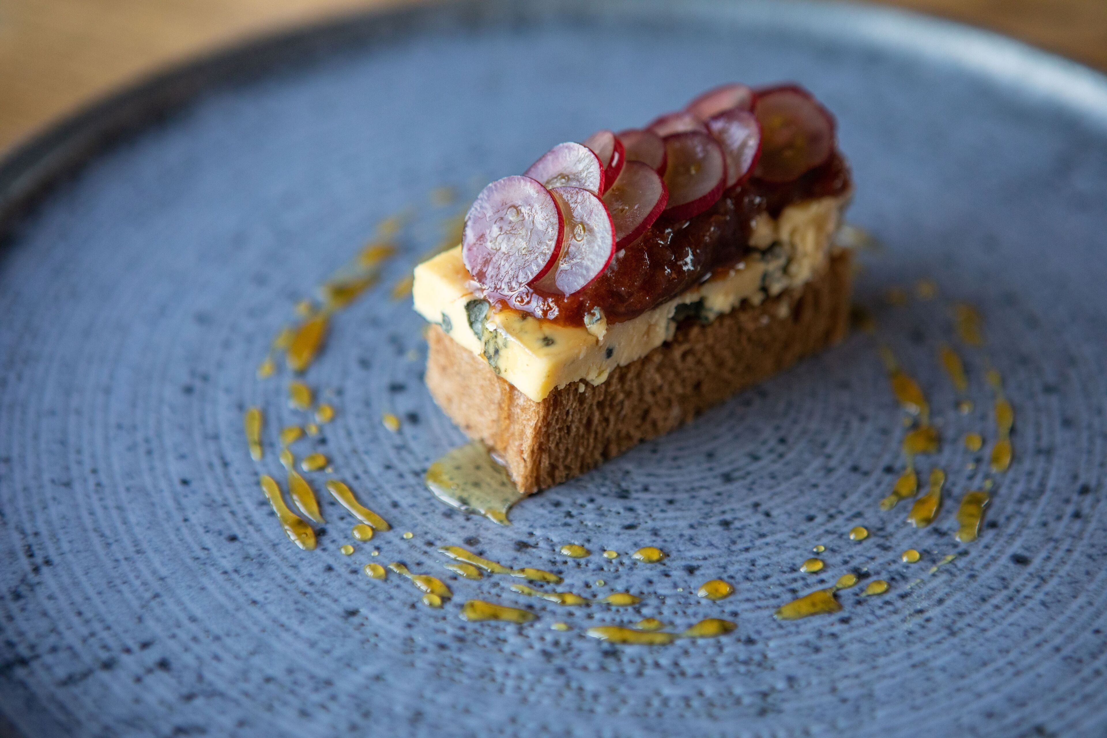 A slice of bread with cheese and radish slices on a blue plate.