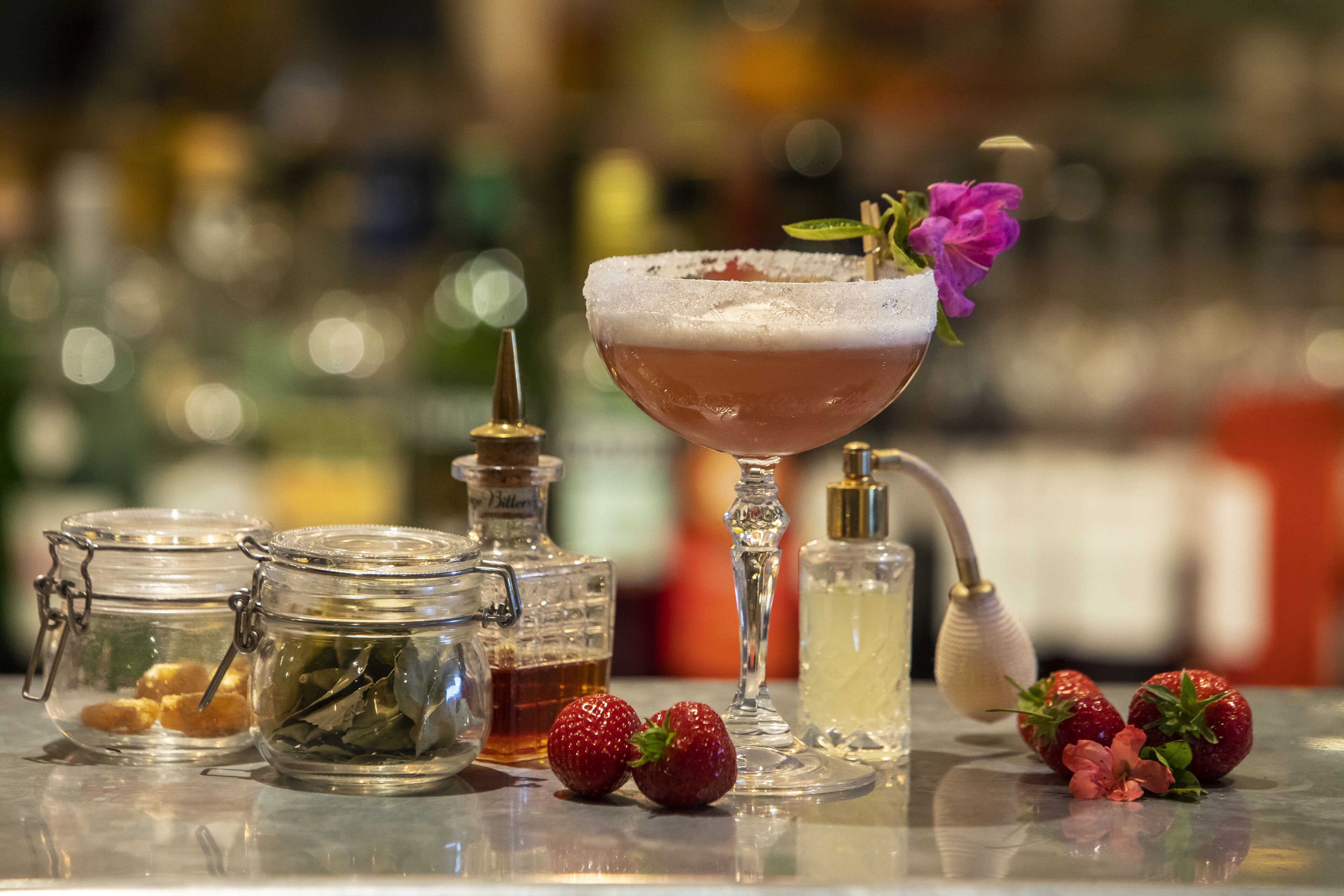 Een barscène met een cocktail, potten augurken en verse aardbeien.