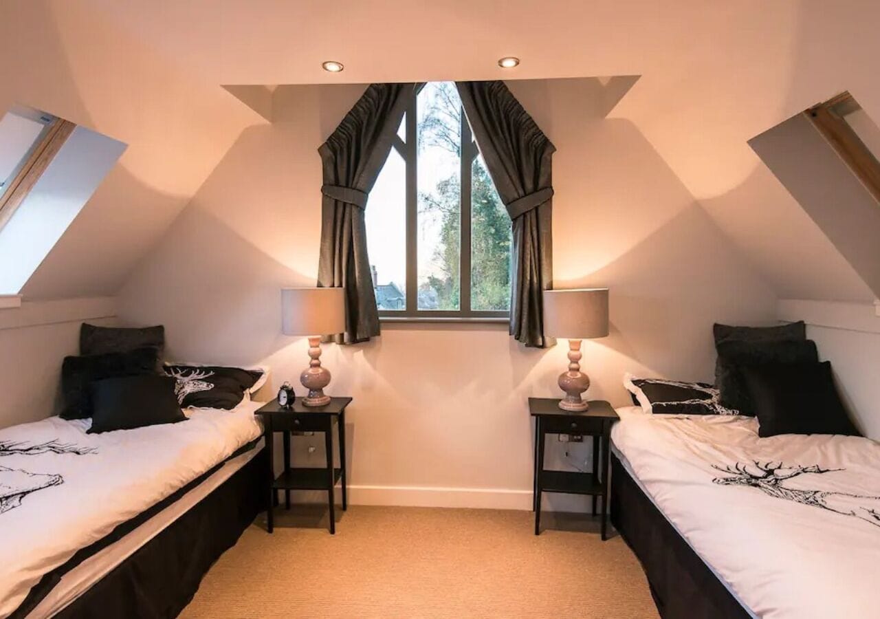 A bedroom with two beds, a window with curtains, and two bedside tables with lamps.