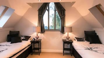 A bedroom with two beds, a window with curtains, and two bedside tables with lamps.