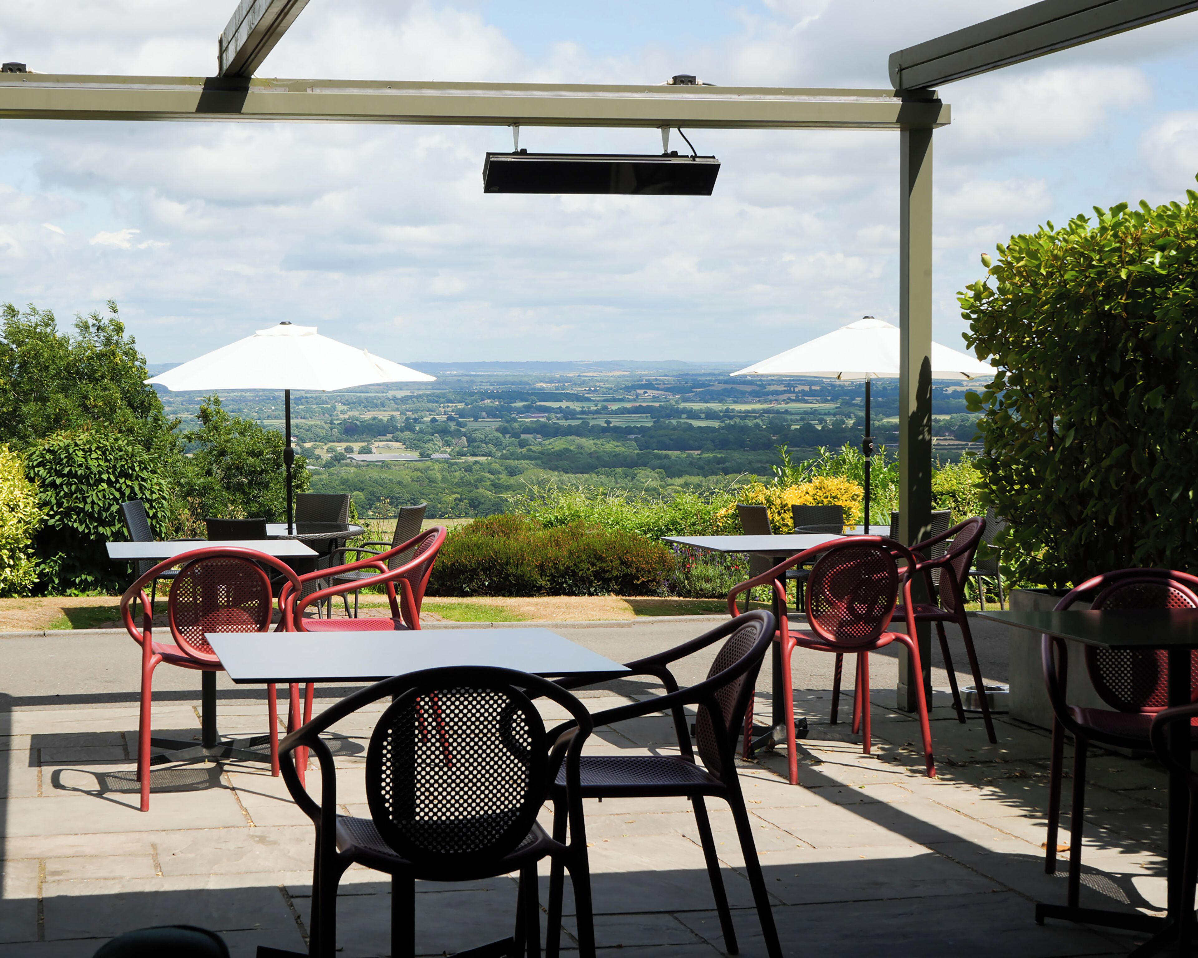 Un patio al aire libre con mesas y sillas, sombrillas blancas y vista al campo.